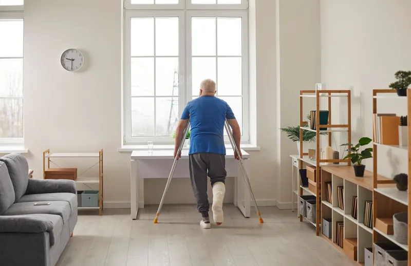 Man with a cast and crutches standing by a window.