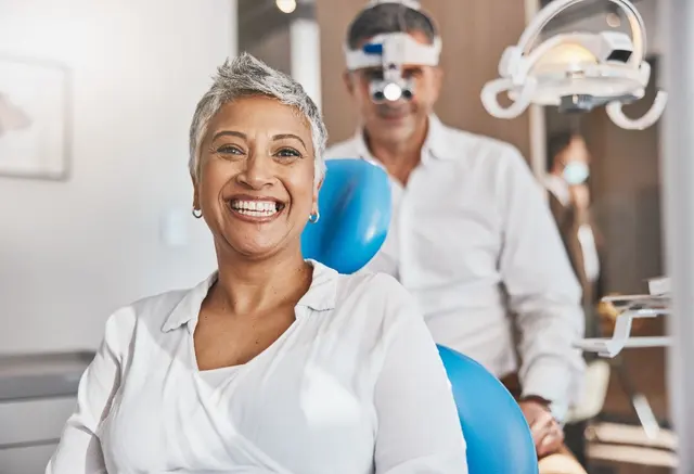 A smiling woman in a dental chair, with a dentist behind her.