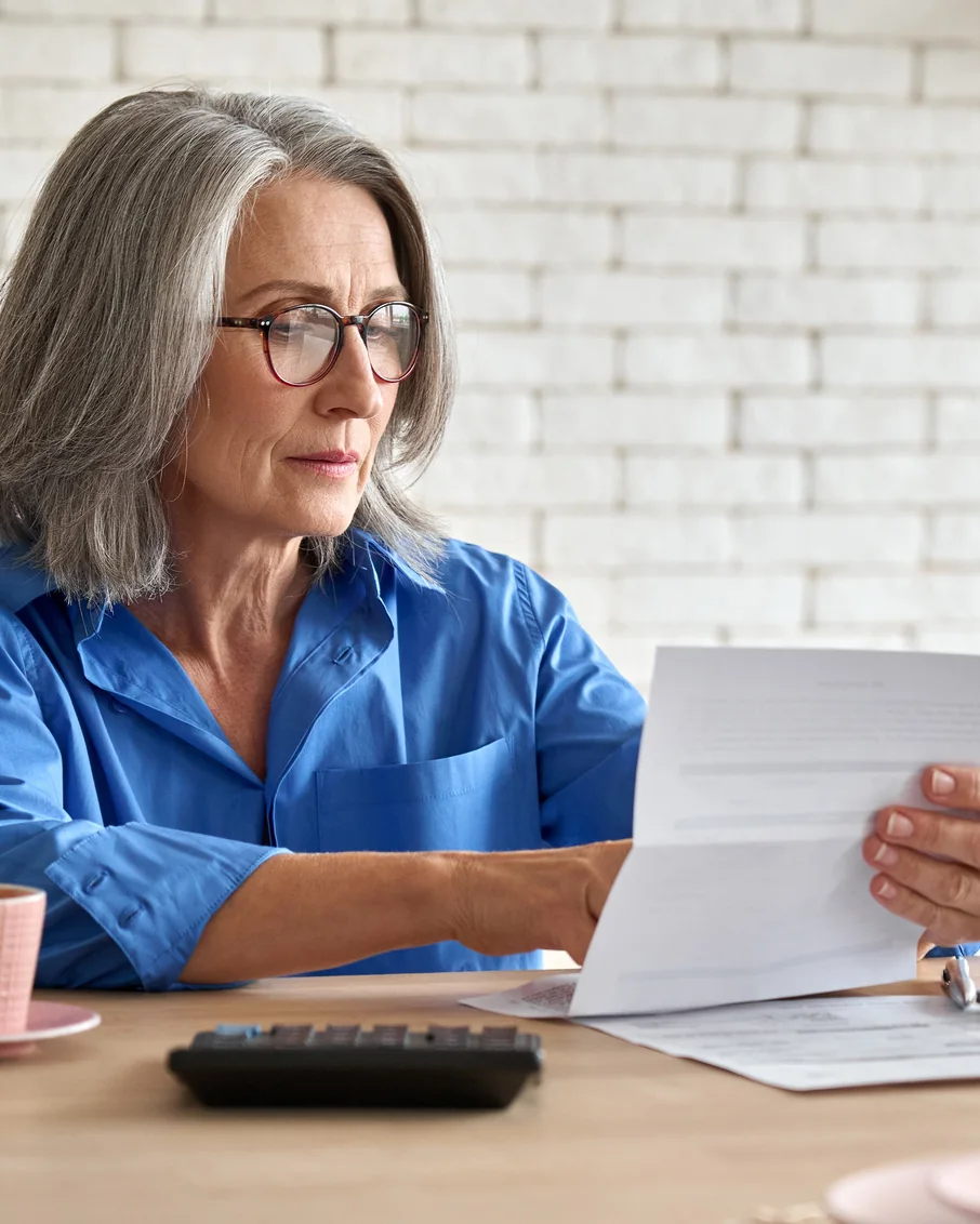 Woman in a blue shirt reviewing a letter from her Medicare plan at her kitchen table.