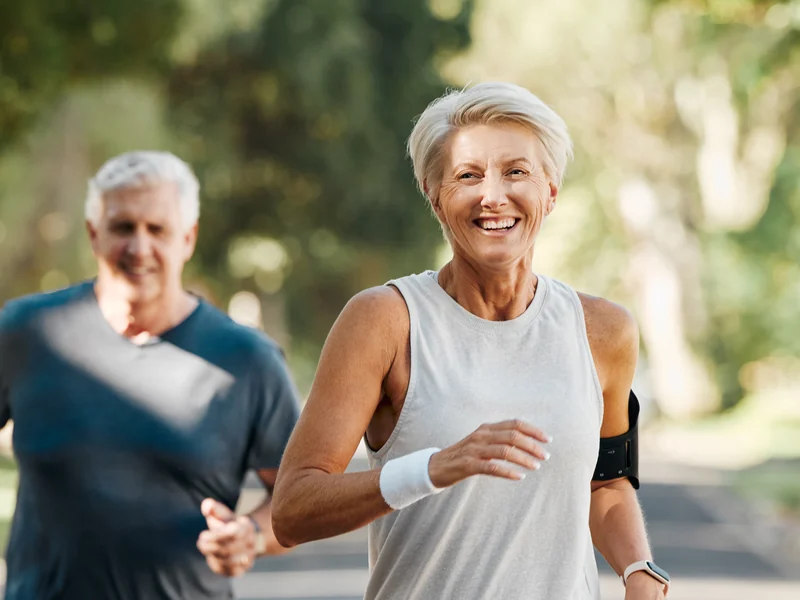 Illustrative photo of an older couple jogging together on a tree-lined road, the woman in front.
