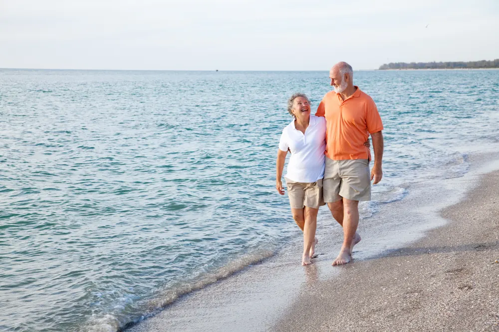 Older couple walking arm in arm along a Florida beach.